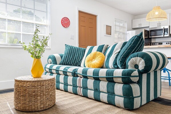 A living room with a striped sofa, a round wicker ottoman, and a yellow vase with green plants. - Lovely 2 BR Condo in Sailboat Bend (Fort Lauderdale)