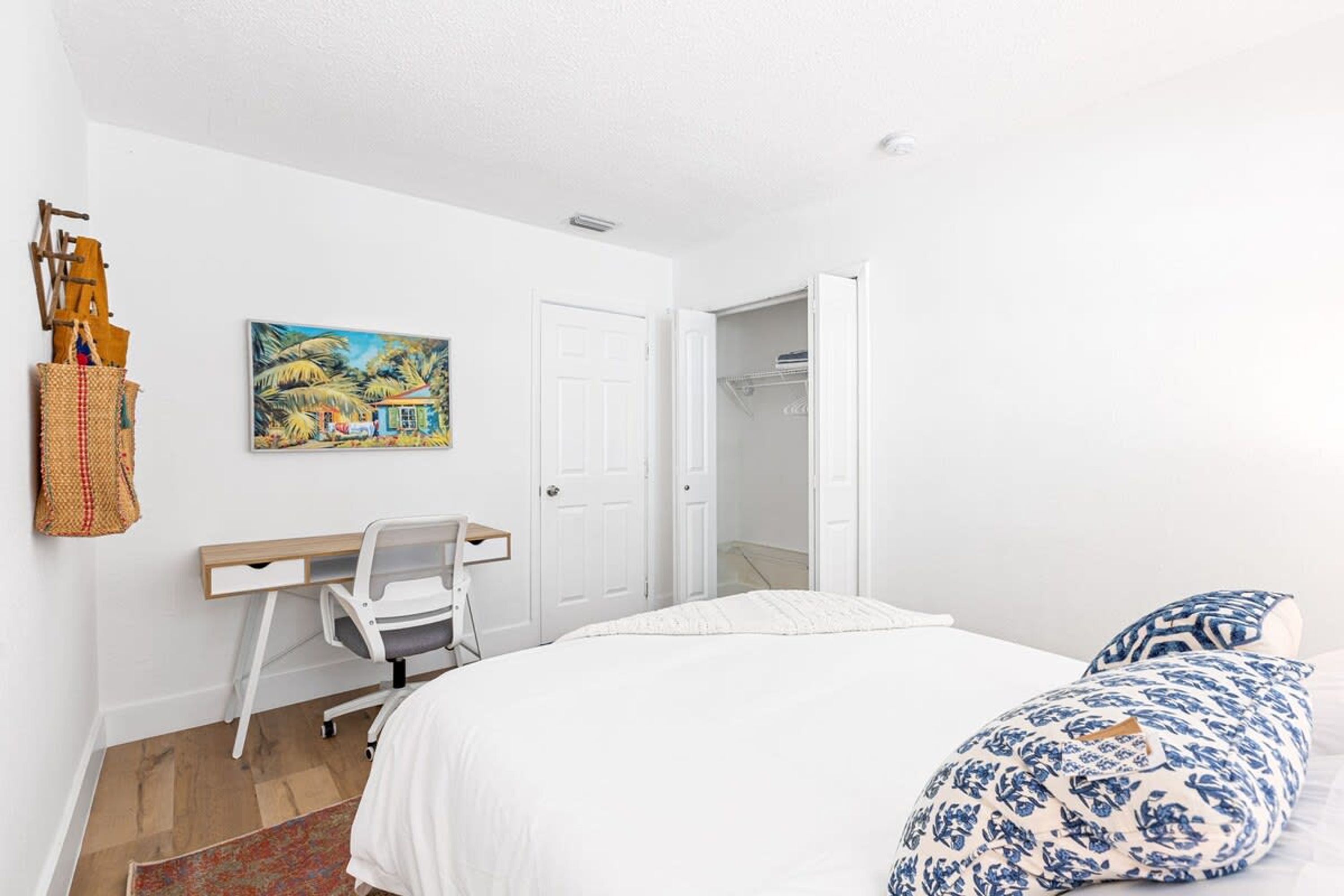 Een slaapkamer met een bed, een bureau, een stoel, een schilderij en een kast.