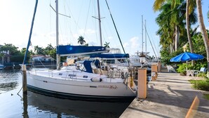 Un port de plaisance où un yacht blanc est amarré au quai, entouré de palmiers et sous un ciel dégagé.
