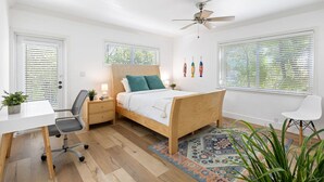 Une chambre à coucher avec un lit en bois, un bureau, une chaise, un ventilateur de plafond et une fenêtre avec des stores.