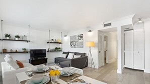 Een moderne woonkamer met een eethoek, grijze banken, een televisie en een gedekte eettafel met borden en glazen.