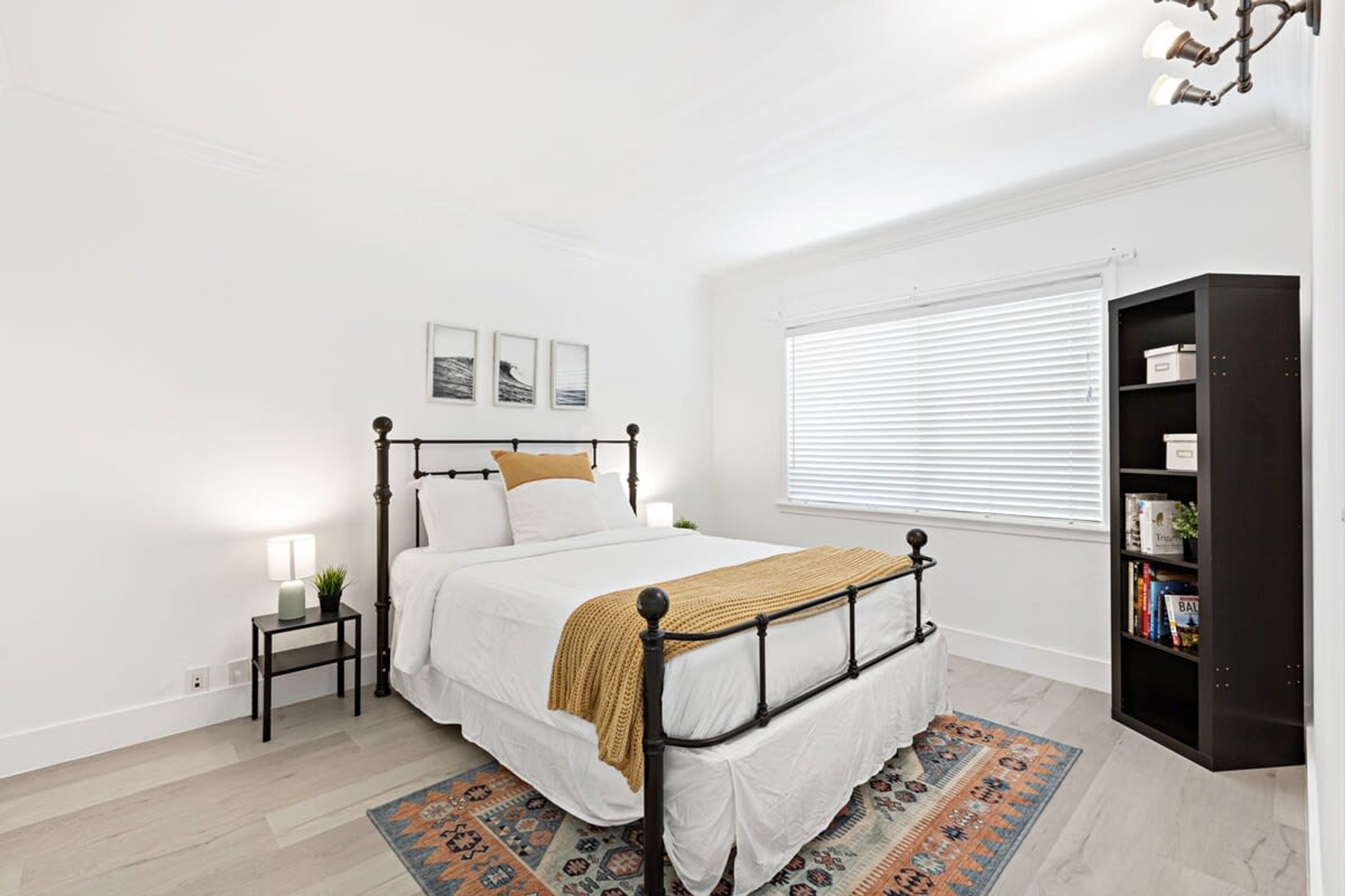 A bedroom with a bed, bedside table, lamp, and a bookshelf.