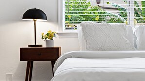 A neatly made bed with white bedding, a small bedside table with a lamp, and a window with blinds. - Spacious Beach Apt in Las Olas Blvd (Fort Lauderdale)