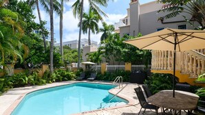 A swimming pool surrounded by palm trees and a covered seating area with a table and chairs. - Spacious Beach Apt in Las Olas Blvd (Fort Lauderdale)