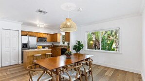 A modern kitchen with white cabinetry, a wooden dining table, and a large window with a view of greenery. - Spacious Beach Apt in Las Olas Blvd (Fort Lauderdale)