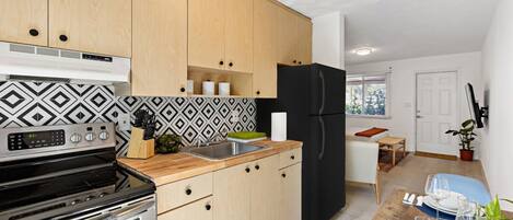 A modern kitchen with wooden cabinets, a black refrigerator, and a dining area with a table set for two.