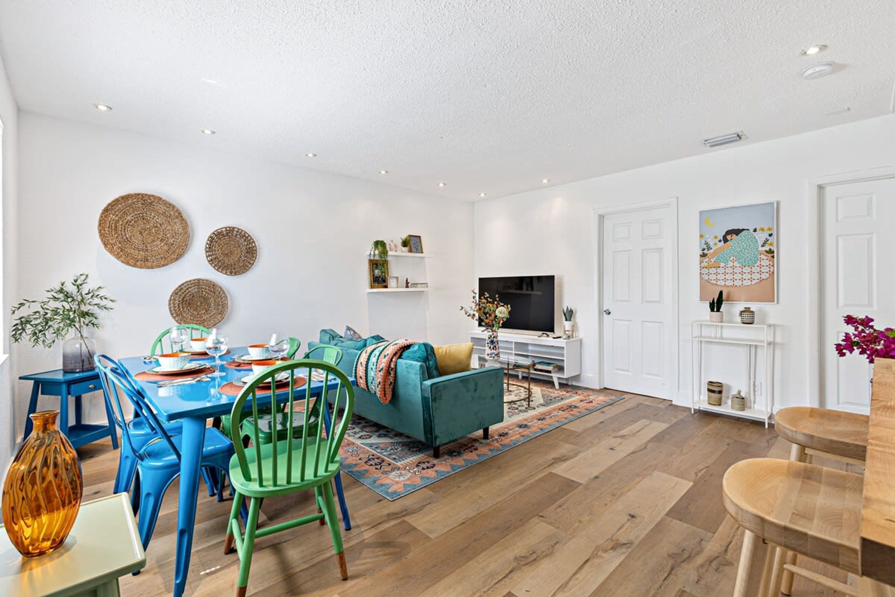 Un salon moderne avec une table à manger bleue, des chaises vertes, un canapé turquoise et un téléviseur à écran plat.