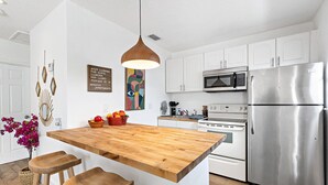 A modern kitchen with white cabinets, a wooden island with stools, stainless steel appliances, and decorative wall art. - Stylish 2 BR Condo - Close to Riverwalk (Fort Lauderdale)