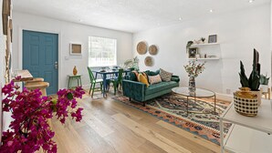 A living room with a teal sofa, wooden flooring, a patterned rug, and a dining area with a table and chairs. - Stylish 2 BR Condo - Close to Riverwalk (Fort Lauderdale)