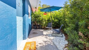 A blue building with a door, a small patio with a chair and umbrella, and a 'Hello Summer' mat. - Stylish 2 BR Condo - Close to Riverwalk (Fort Lauderdale)