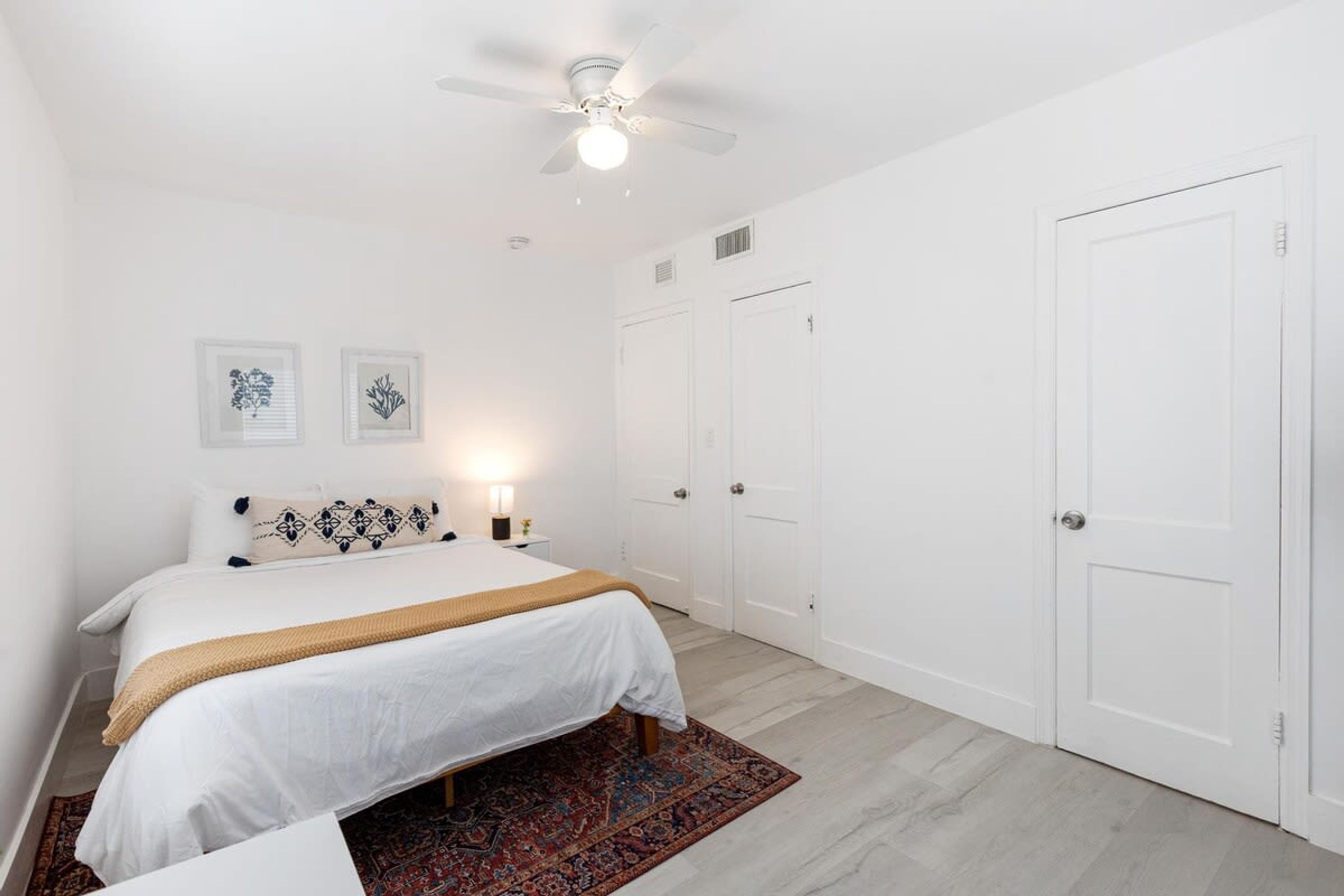 Une chambre à coucher avec un lit, un ventilateur de plafond, deux portes et une table de chevet avec une lampe.