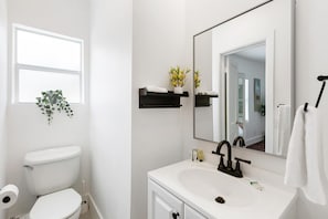 Een badkamer met een wit toilet, een witte wastafel, een spiegel en een raam.
