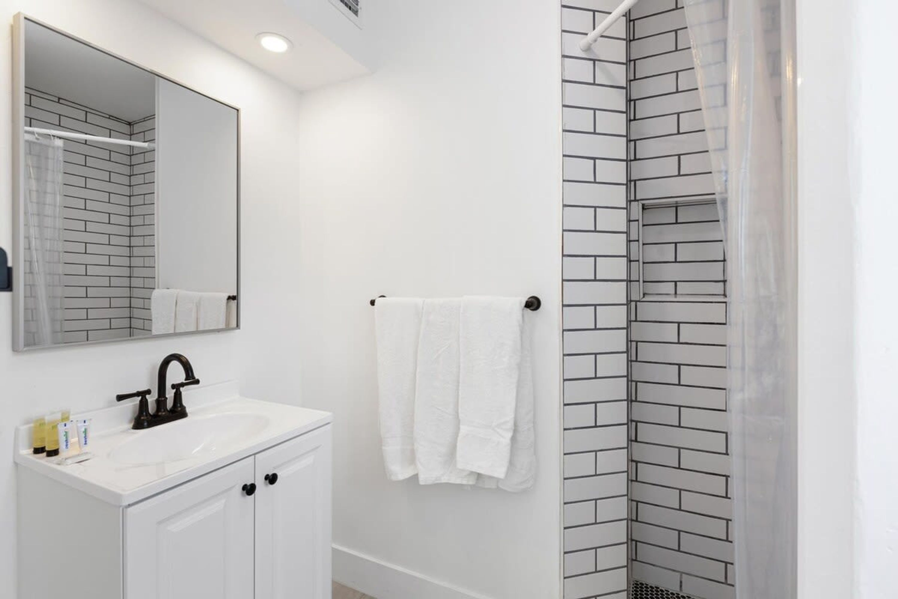 A bathroom with a white sink, black faucet, and a mirror above it. There is a white towel hanging on a towel rack.
