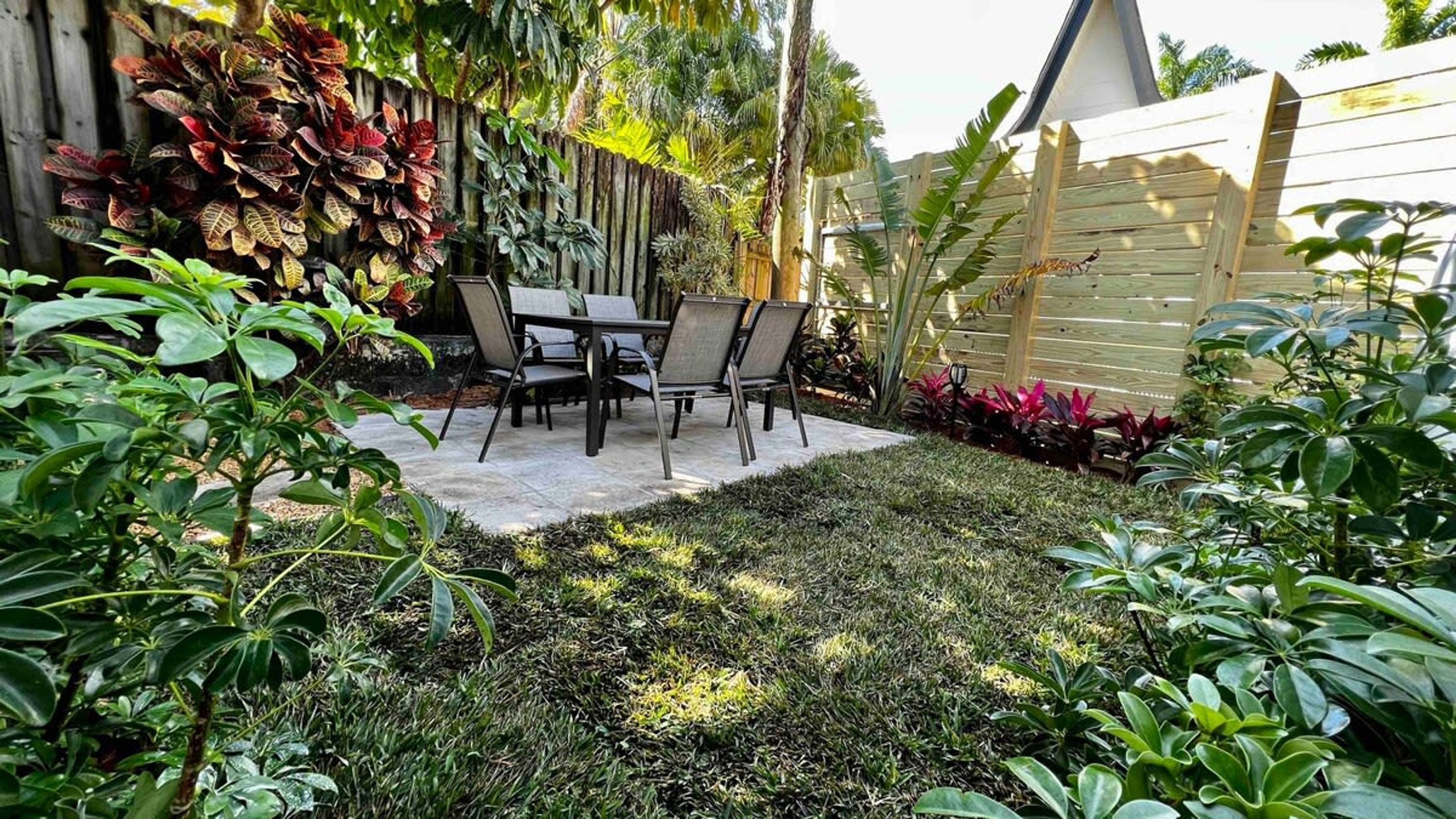A patio area with a table and chairs, surrounded by lush greenery and a wooden fence.