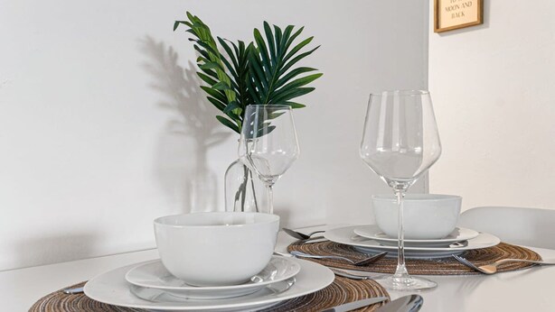 A dining table set with white plates, bowls, and wine glasses, accompanied by a decorative plant and a framed quote on the wall. - The Perfect Escape Lake Ridge (Fort Lauderdale)