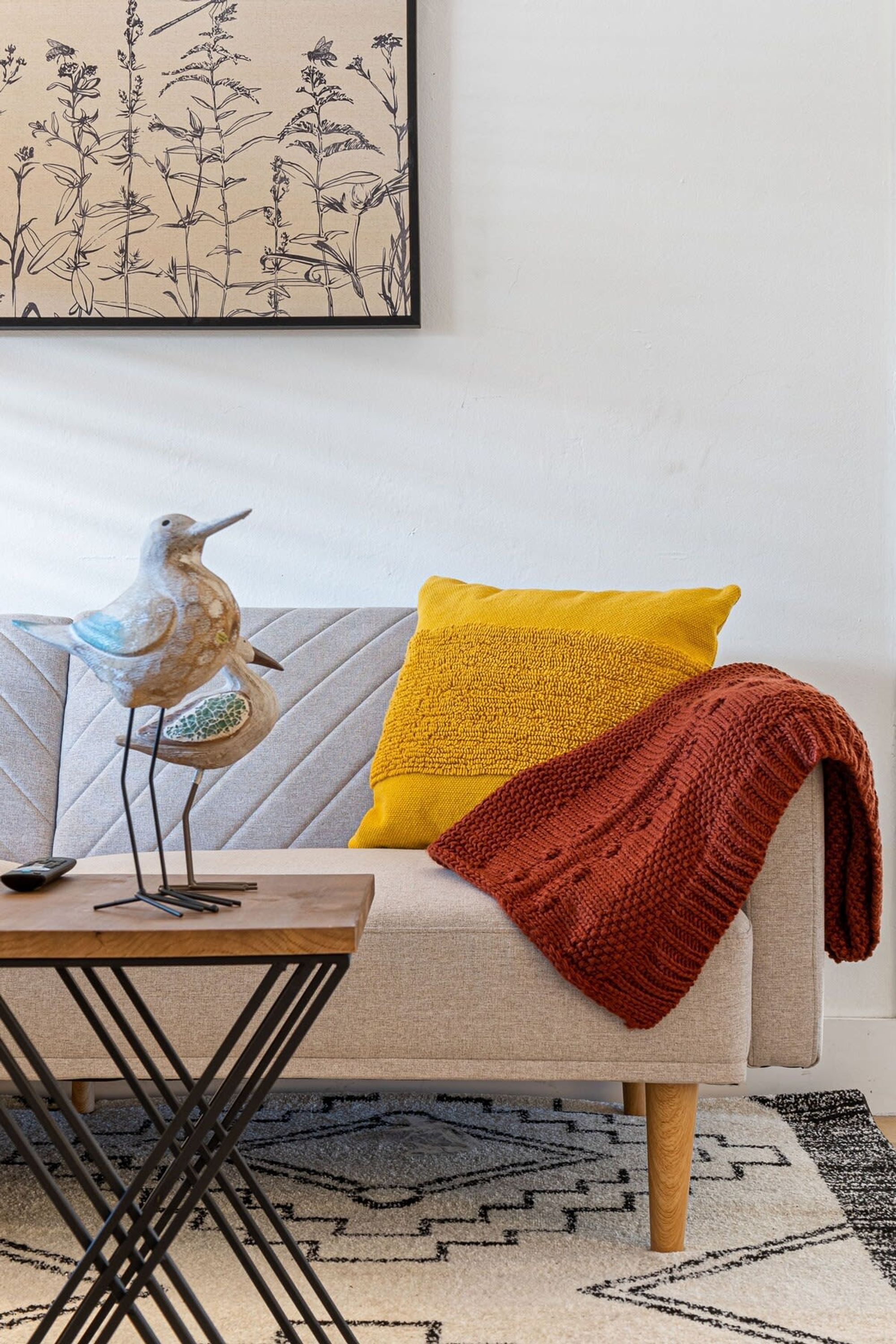 Una sala de estar moderna con un sofá, una manta de colores, una escultura decorativa de un pájaro y una alfombra estampada.