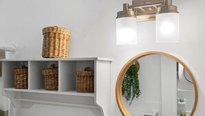 A bathroom with a white vanity, wicker baskets on the shelf, a round mirror with a gold frame, and a wall-mounted light fixture. - The Perfect Escape Lake Ridge (Fort Lauderdale)