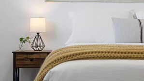 A neatly made bed with white linens, a beige knitted throw, and a bedside lamp with a geometric base. - The Perfect Escape Lake Ridge (Fort Lauderdale)