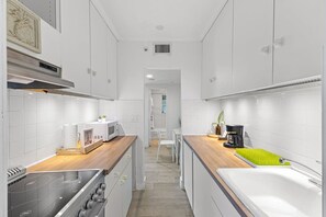 A narrow kitchen with white cabinets, a stove, a microwave, and a sink. - Delight and Cozy Apt Close to Las Olas the Beach (Fort Lauderdale)