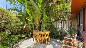 Un patio con una mesa y sillas de madera, rodeado de abundante follaje y una valla de madera.