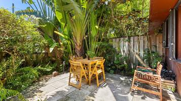Une terrasse avec une table et des chaises en bois, entourée d’une végétation luxuriante et d’une clôture en bois.
