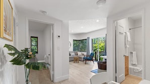 Un interior moderno con piso de madera, una silla blanca, una planta y vistas a un balcón con vegetación.