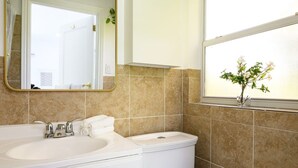Une salle de bain avec un lavabo blanc, un miroir avec un cadre doré, des toilettes et une fenêtre avec une plante.
