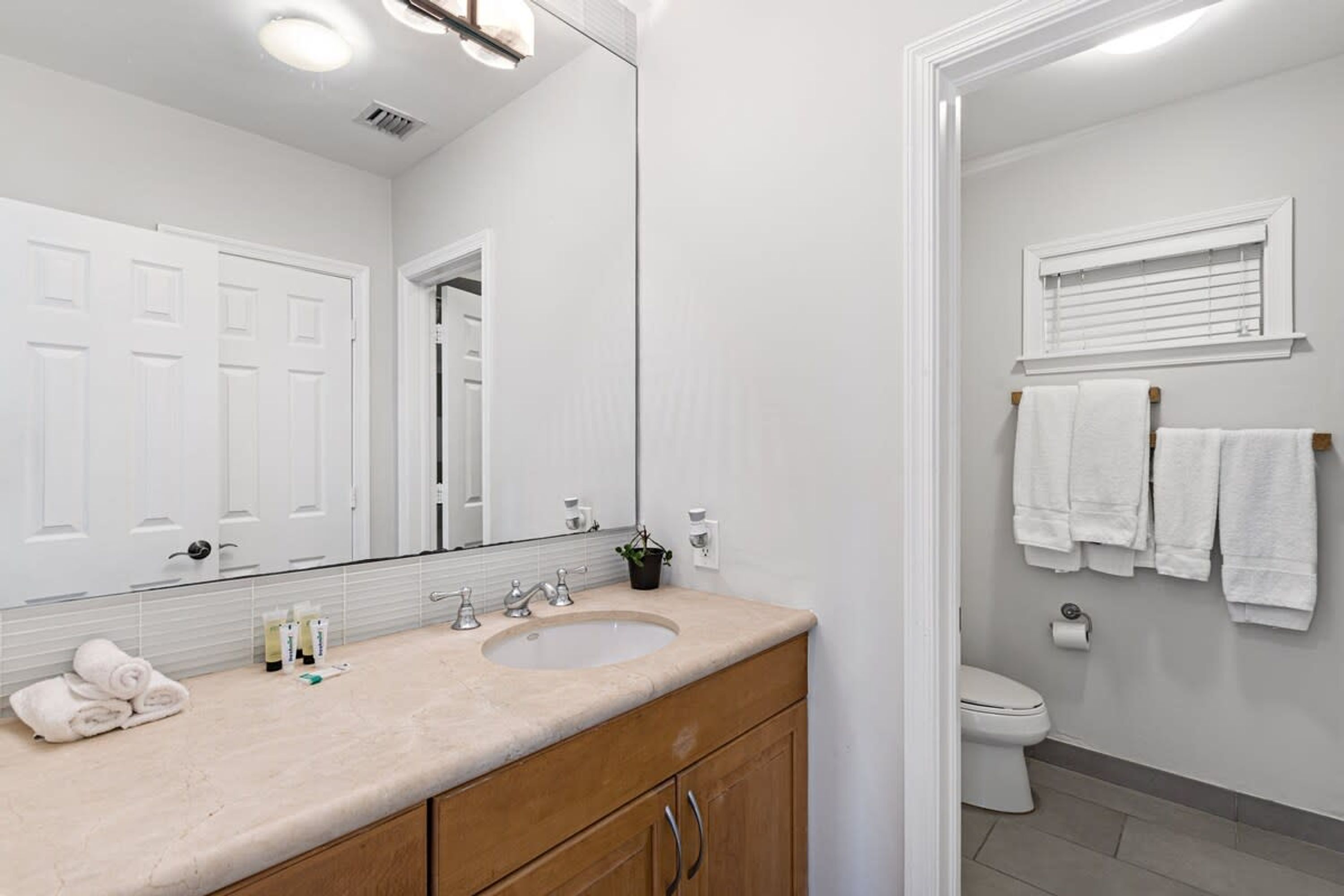 Une salle de bain moderne avec un meuble-lavabo à deux vasques, un grand miroir et des toilettes dotées d’un porte-serviettes.