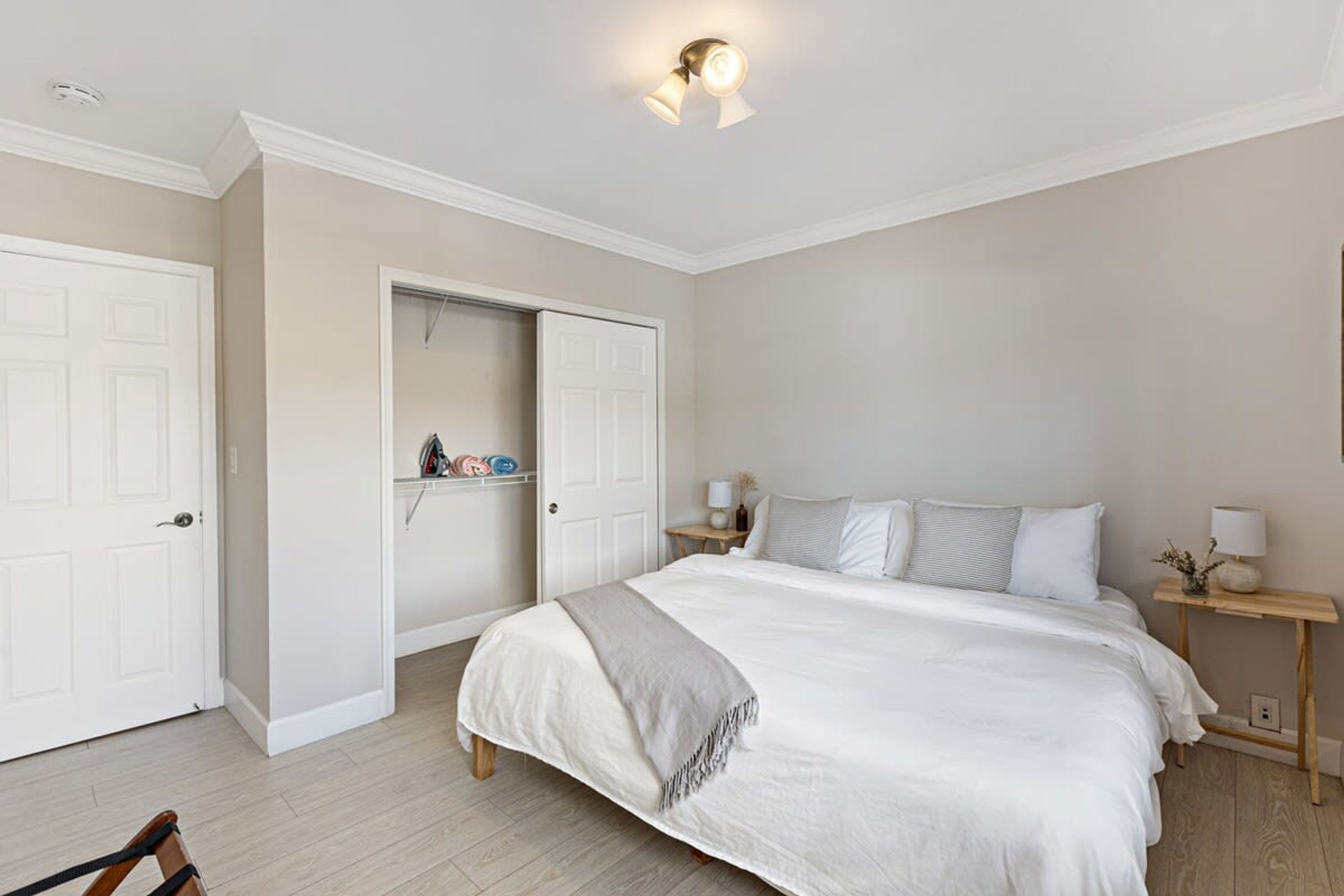 Quarto com uma cama grande, mesa de cabeceira com abajur e guarda-roupa.