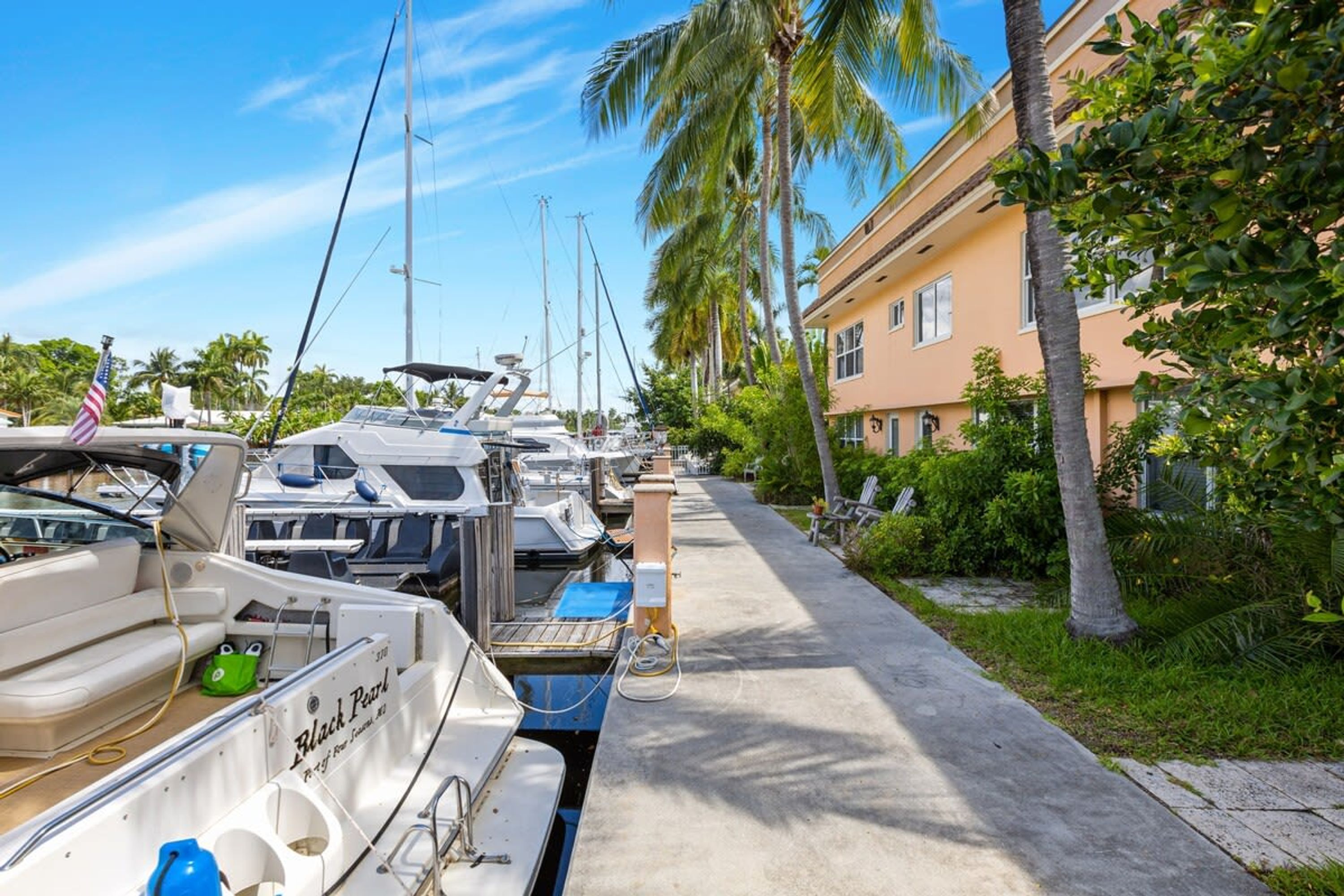 Un port de plaisance où sont amarrés plusieurs bateaux, un trottoir et un bâtiment à la façade de couleur claire.