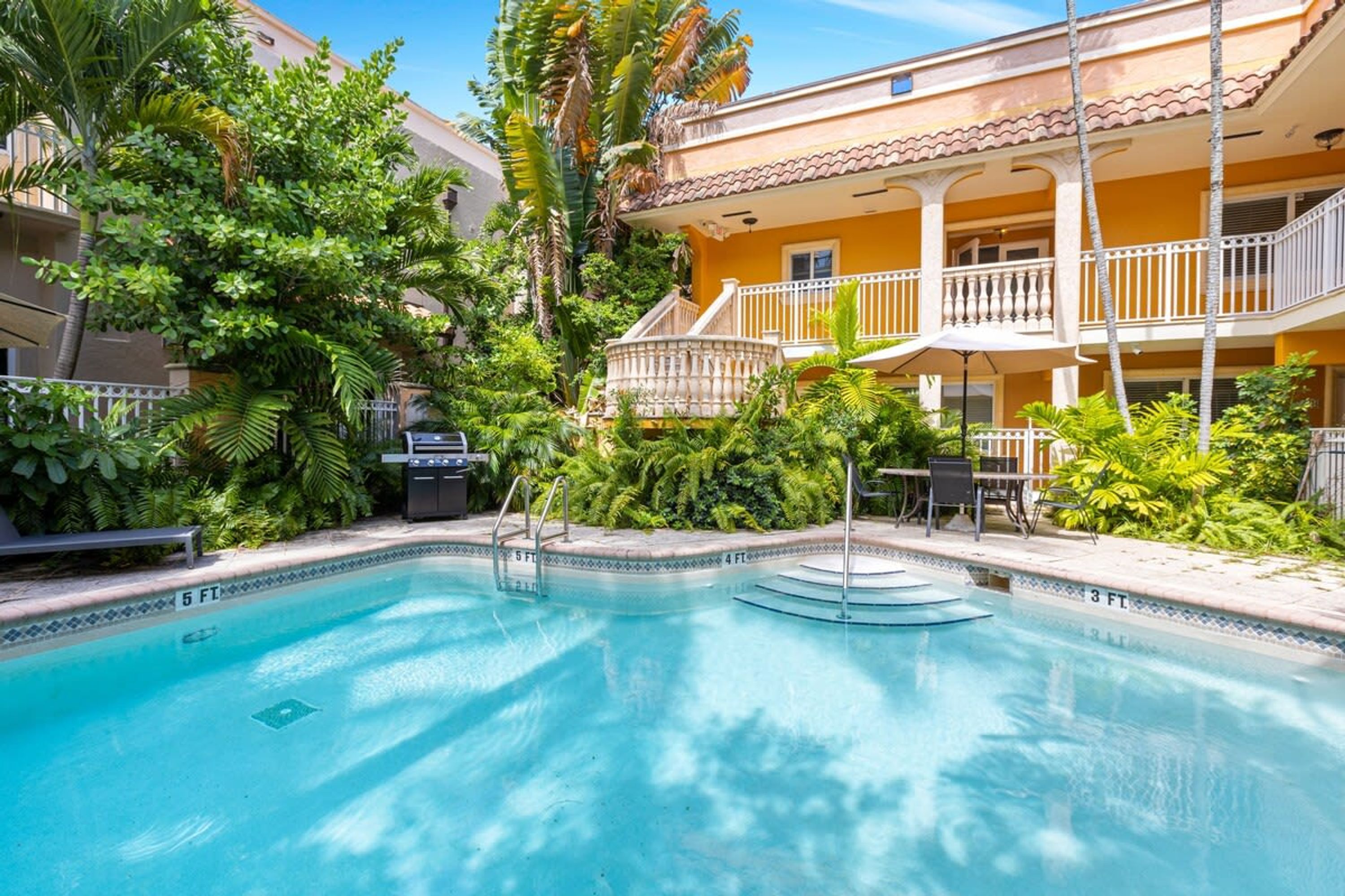 A swimming pool surrounded by lush greenery and a multi-story building with balconies.