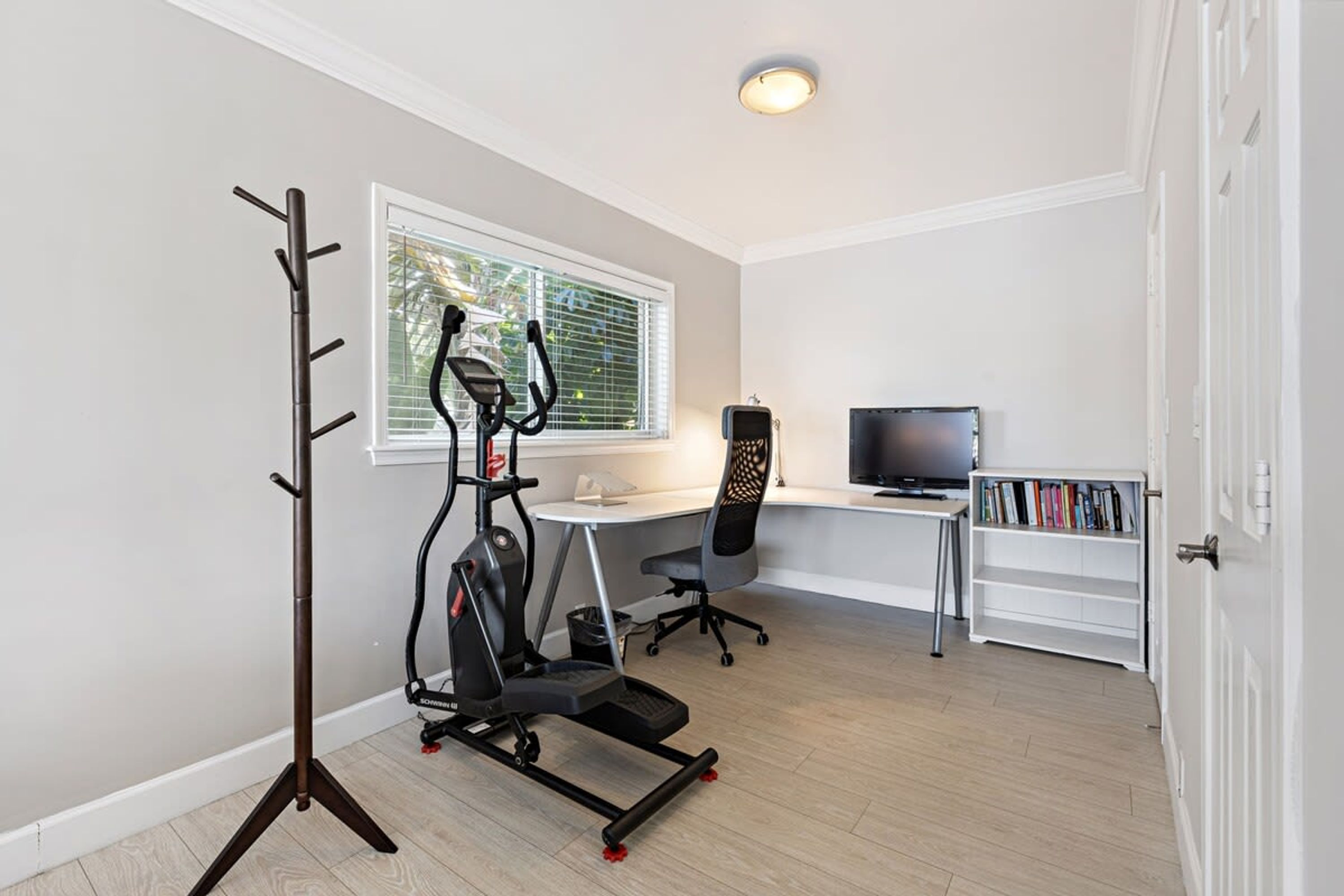 A room with a treadmill, a desk, a chair, a television, and a bookshelf.