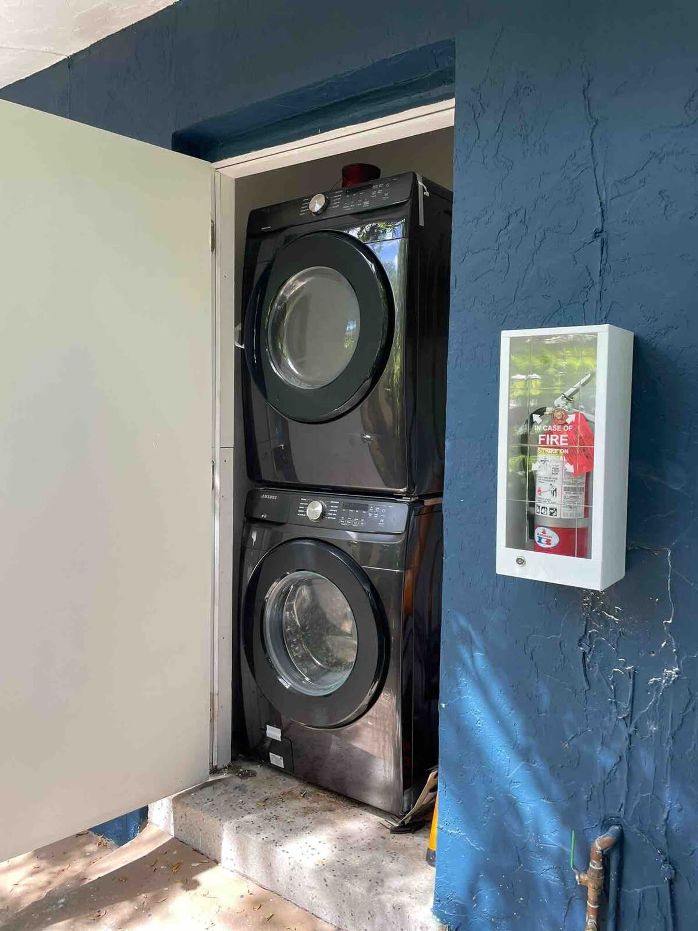 A laundry room with two stacked front-loading washers and a fire extinguisher mounted on the wall.