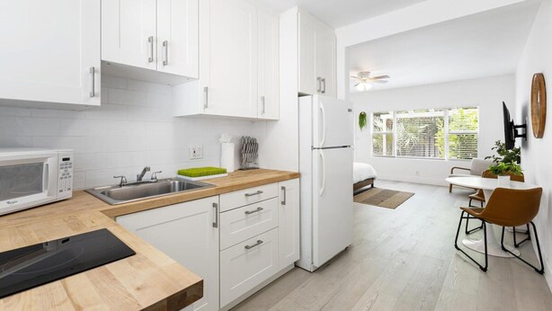 A modern kitchen with white cabinets, a microwave, and a sink. There is a dining area with a table and chairs.