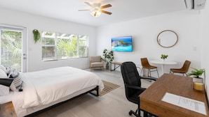 A modern hotel room with a bed, desk, chairs, and a ceiling fan.