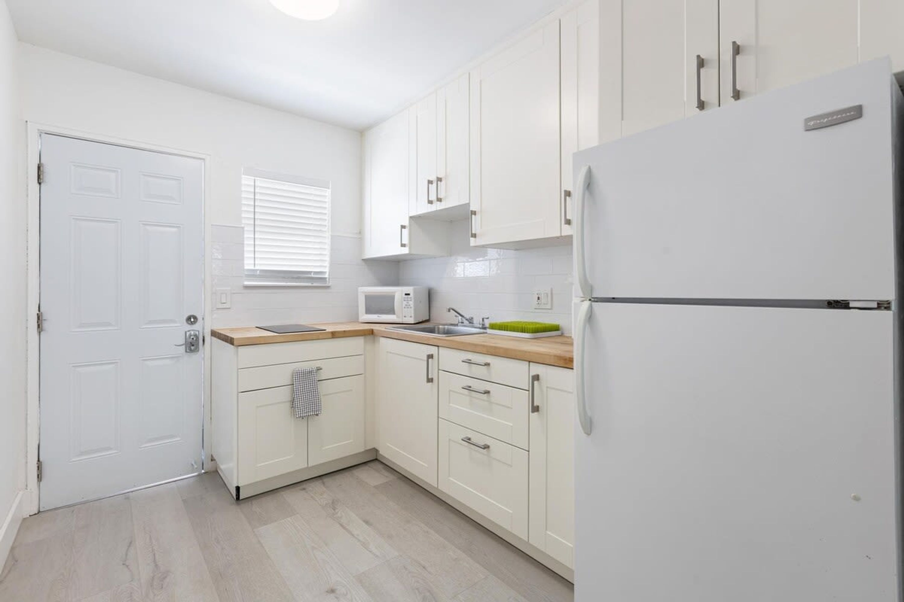 A compact kitchen with white cabinets, a microwave, a sink, and a refrigerator.
