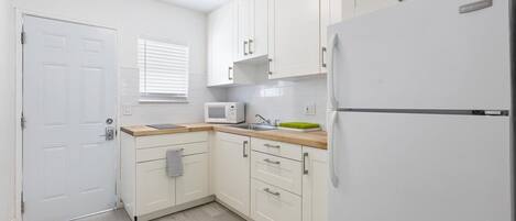 A compact kitchen with white cabinets, a microwave, a sink, and a refrigerator.