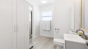 A modern bathroom with white cabinetry, a toilet, a sink, and a window.