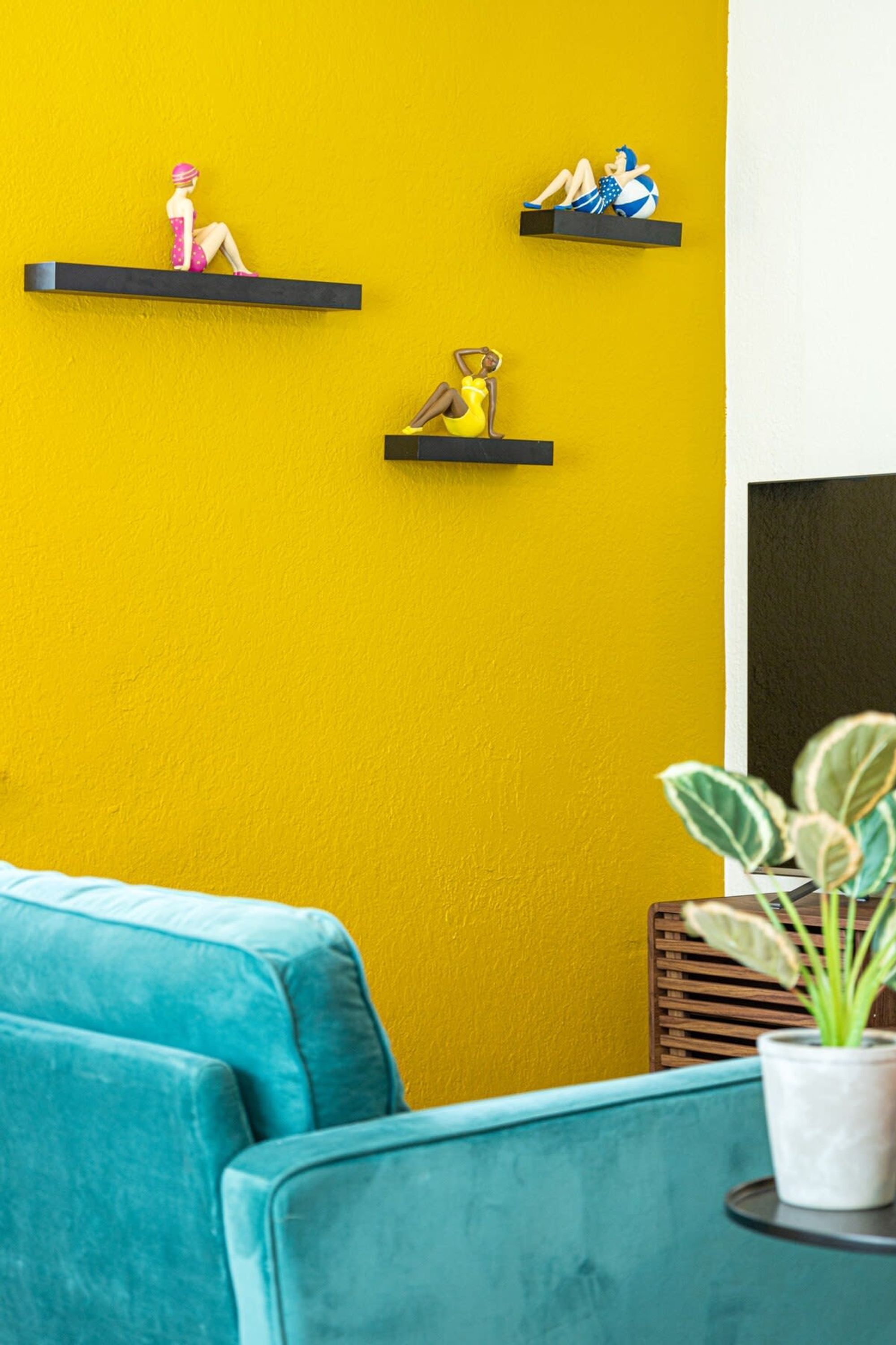 Une pièce avec des chaises de couleur turquoise, un mur jaune et des objets décoratifs disposés sur des étagères.