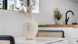 Ett modernt kök med en vit bänkskiva, en stor vas med torkade blommor, en svart kran och en krukväxt.