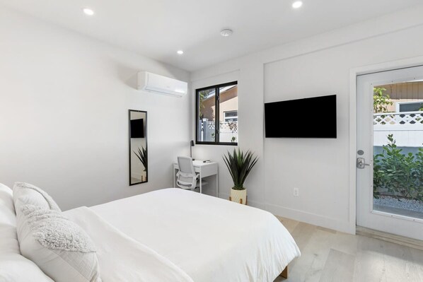 A modern bedroom with a bed, a desk, a chair, a TV, and a door leading to a balcony. - Mango House Dania Beach (Dania Beach)
