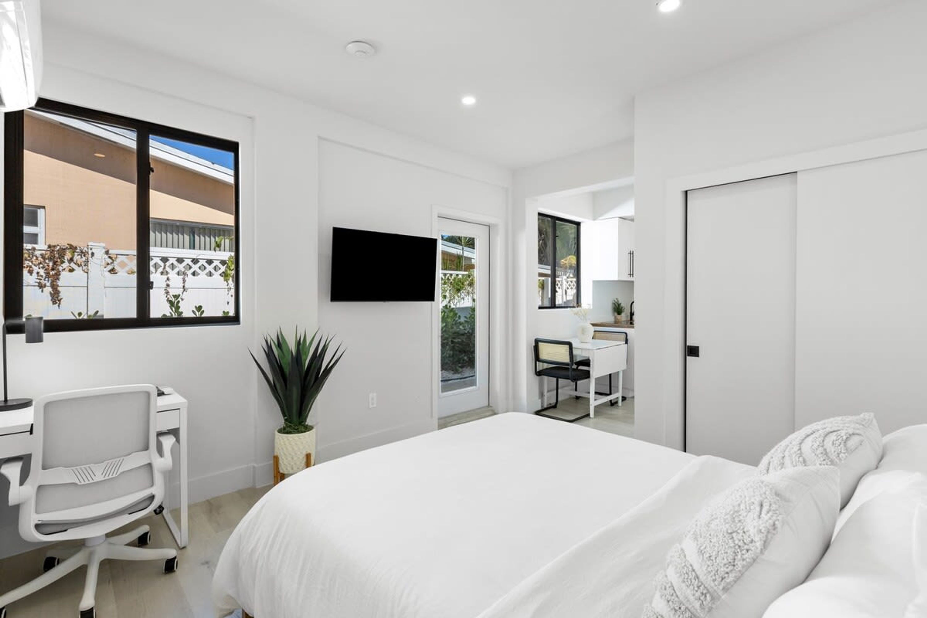 Un dormitorio moderno con una cama grande, un escritorio y una silla. Hay un televisor montado en la pared y una planta en maceta sobre el escritorio.