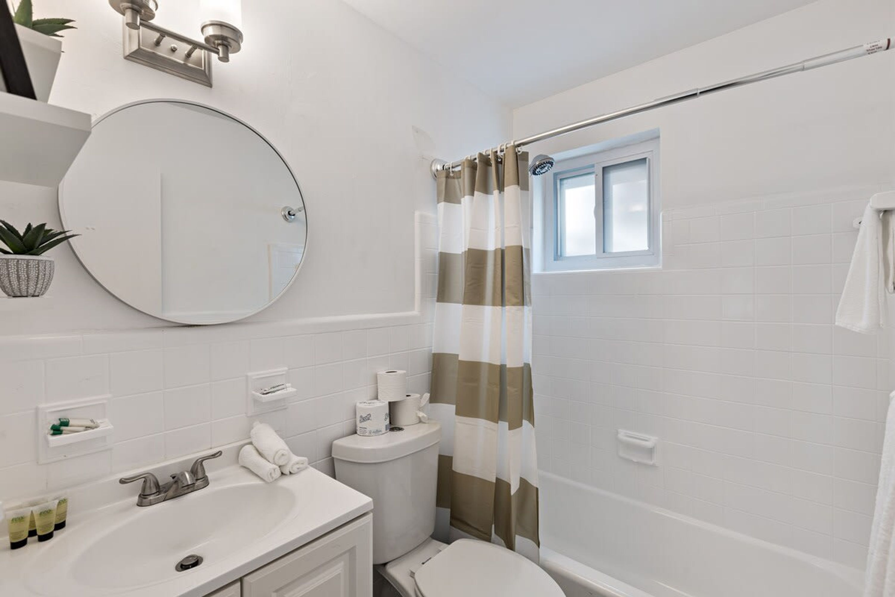 Een badkamer met een ronde spiegel, een witte wastafel, toilet en douchegordijn.