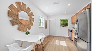 A modern kitchen with white cabinetry, a stainless steel refrigerator, and a sunburst mirror on the wall. - Morning Sunshine Sailboat Bend (Fort Lauderdale)