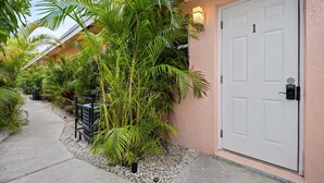 A pathway leading to a white door with a keypad lock, surrounded by lush tropical plants and a small garden area. - Morning Sunshine Sailboat Bend (Fort Lauderdale)