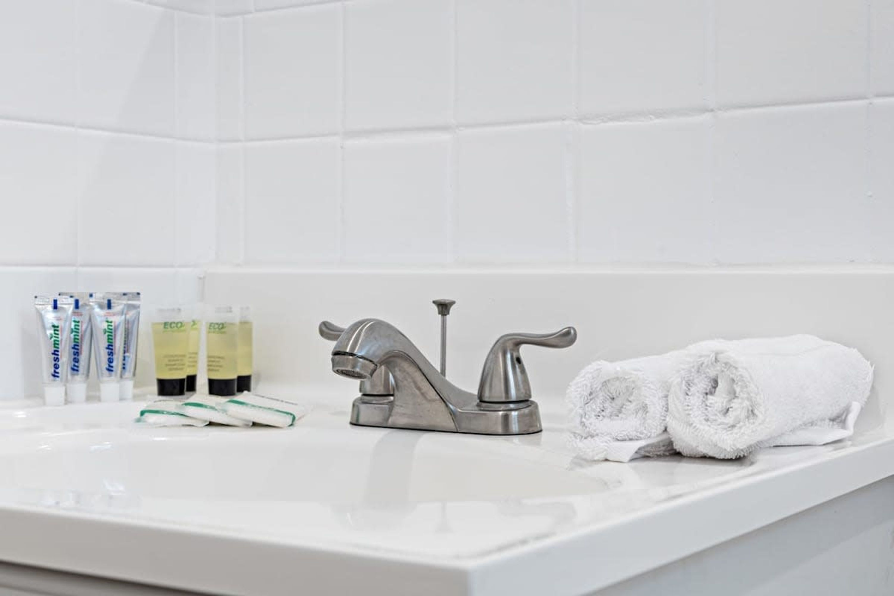 Et badeværelse med en hvid vask, en sølvarmatur og toiletartikler, herunder frisk mynte tandpasta og miljøvenlige produkter.