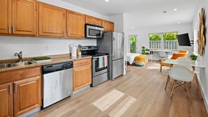 A modern kitchen with wooden cabinets, stainless steel appliances, and a dining area with a white table and yellow chairs. - Morning Sunshine Sailboat Bend (Fort Lauderdale)