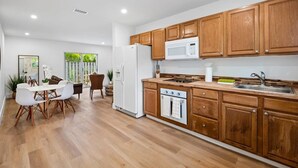 A modern kitchen with wooden cabinets, a white refrigerator, a microwave, and a stove. There is a dining area with a white table and chairs. - Sailors Rest Sailboat Bend (Fort Lauderdale)