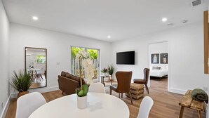 A modern living room with a round dining table, white chairs, a sofa, and a TV mounted on the wall. - Sailors Rest Sailboat Bend (Fort Lauderdale)