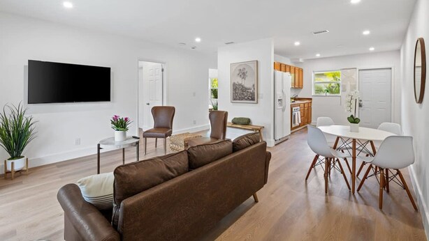 A modern living room with a brown sofa, a dining table with chairs, a flat-screen TV mounted on the wall, and a kitchen area in the background. - Sailors Rest Sailboat Bend (Fort Lauderdale)